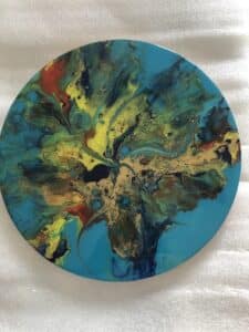 Peinture abstraite fluide sur canevas circulaire aux tourbillons turquoise, jaunes et rouges éclatants.