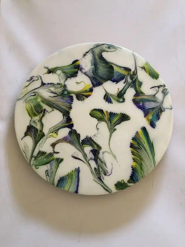 Plat rond blanc avec motifs abstraits de plumes fluides vert, bleu et violet, style peinture acrylique artistique.