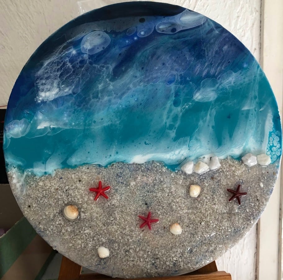 Art en résine circulaire : plage aux vagues bleues, sable blanc, étoiles de mer rouges et coquillages réalistes.