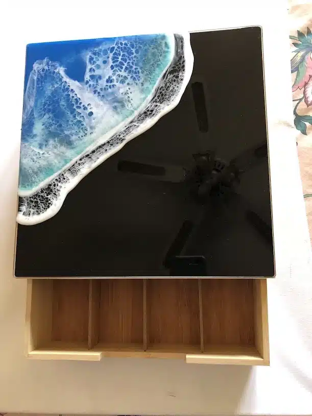 Boîte à bijoux en bois avec couvercle en résine effet vagues de l'océan bleu et blanc sur fond noir brillant.
