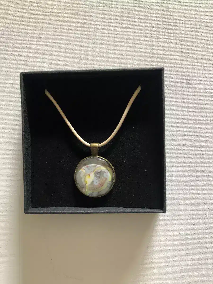 Collier pendentif aux motifs abstraits colorés dans un écrin noir avec cordon beige.
