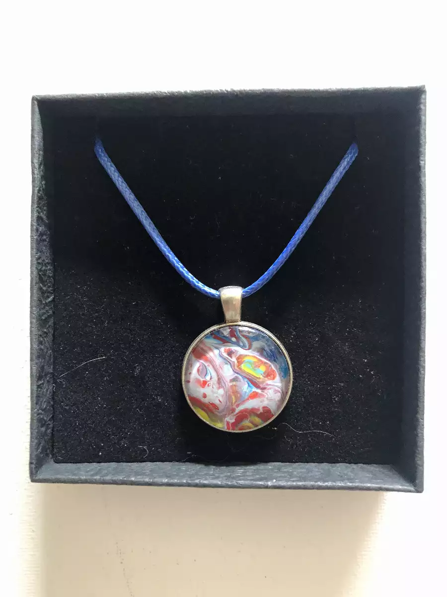Pendentif rond à motif abstrait multicolore sur cordon bleu dans son coffret cadeau noir texturé.