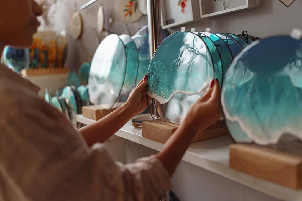 Art en résine époxy : vagues d'océan turquoise sur bois Artiste tenant une création en résine effet vagues d'océan turquoise et blanc sur un socle en bois naturel.
