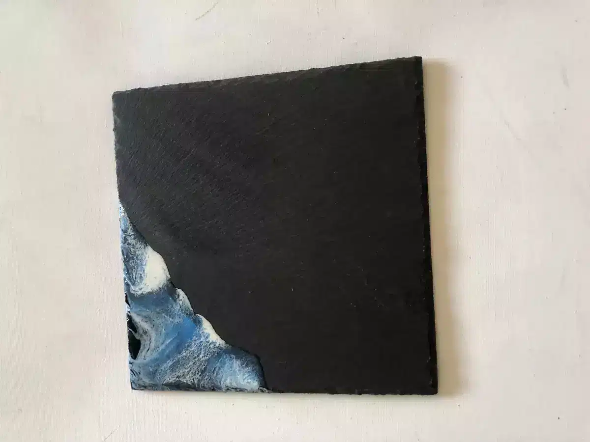 Dessous de plat carré en ardoise noire avec motif vagues en résine époxy bleue et blanche.