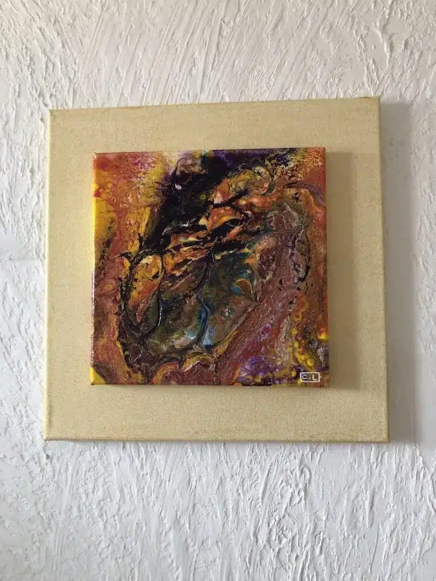 Peinture abstraite fluide jaune et orange montée sur toile beige, mur texturé blanc. Signée C.L.