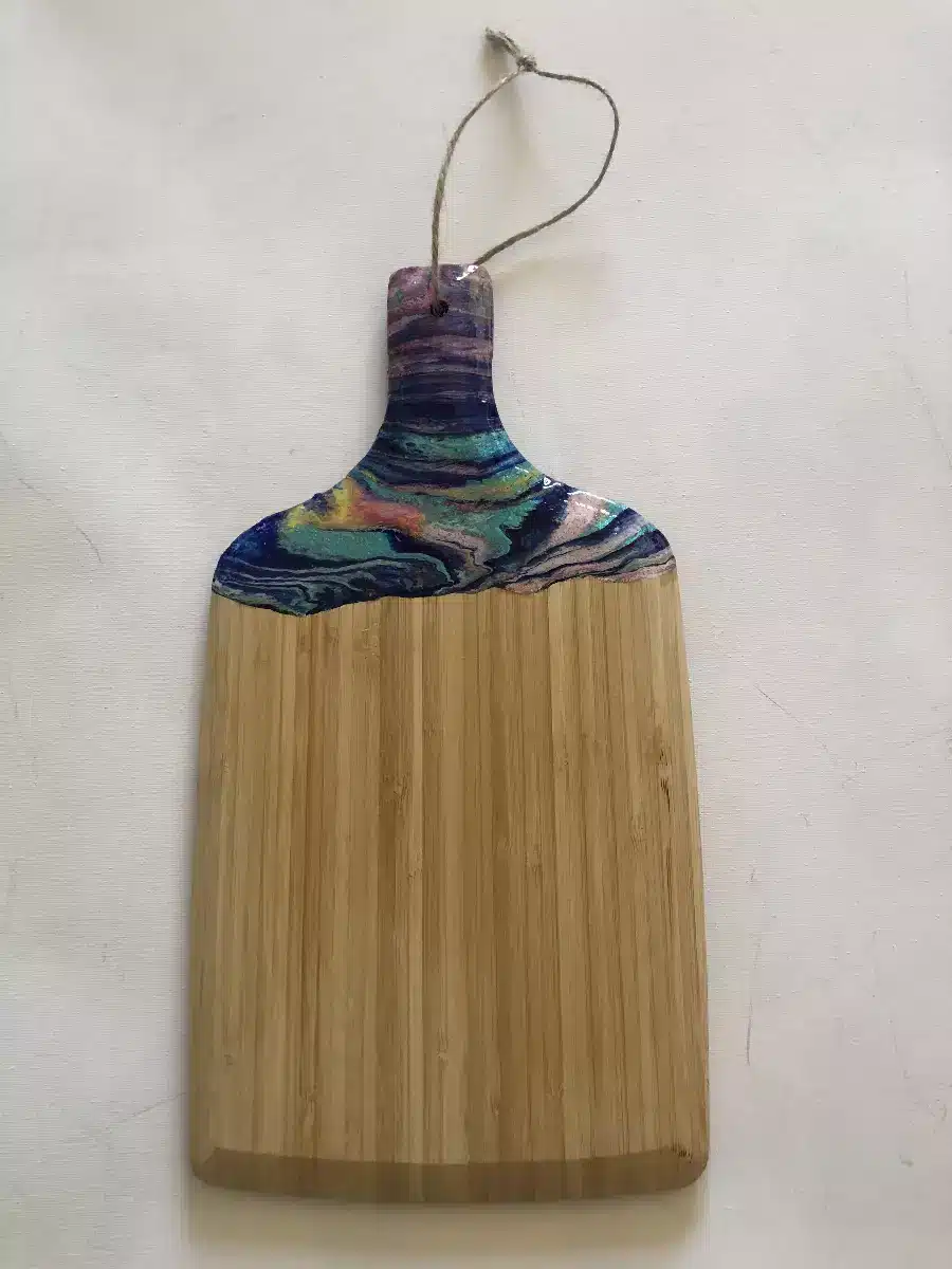 Planche à découper en bambou décorée d'un motif artistique en résine marbrée colorée avec lien en ficelle.