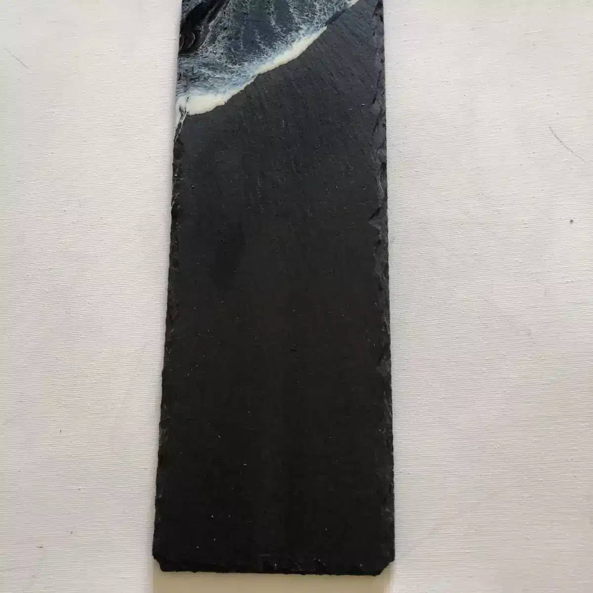 Plateau en ardoise noire rectangulaire orné d'une vague en résine époxy bleue et blanche aux bords ciselés.