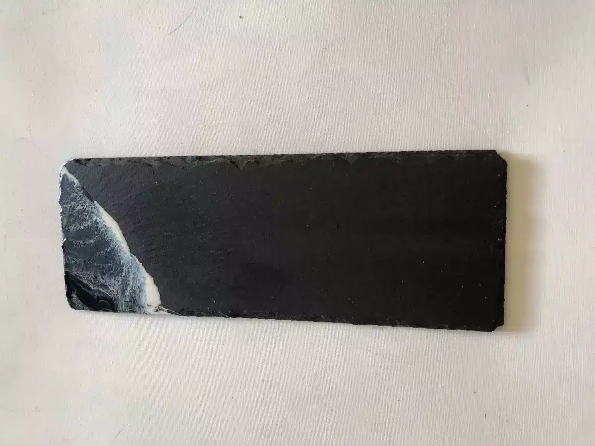 Plateau en ardoise noire avec décor en résine époxy représentant des vagues de l'océan sur le côté gauche.