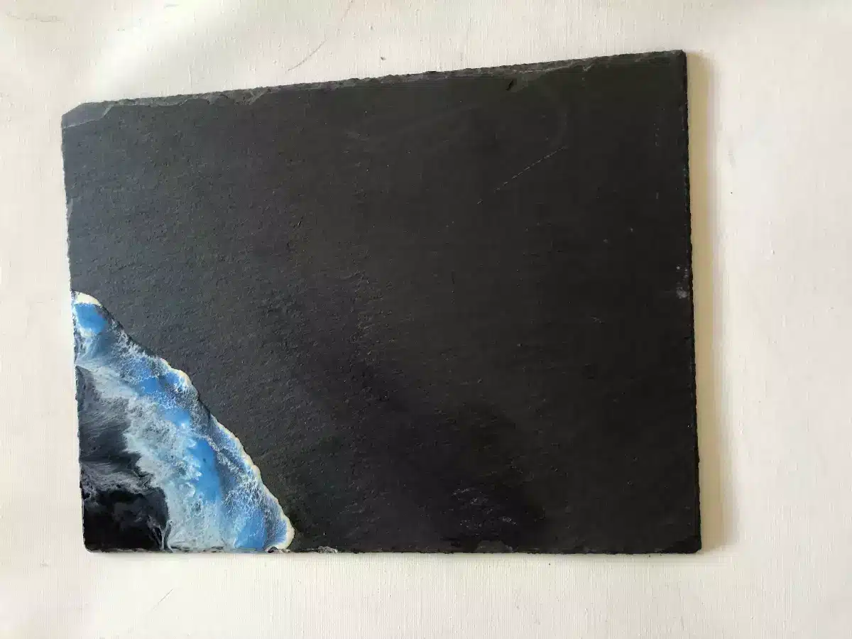 Plateau en ardoise noire avec vague en résine bleue et blanche effet océan dans le coin inférieur.