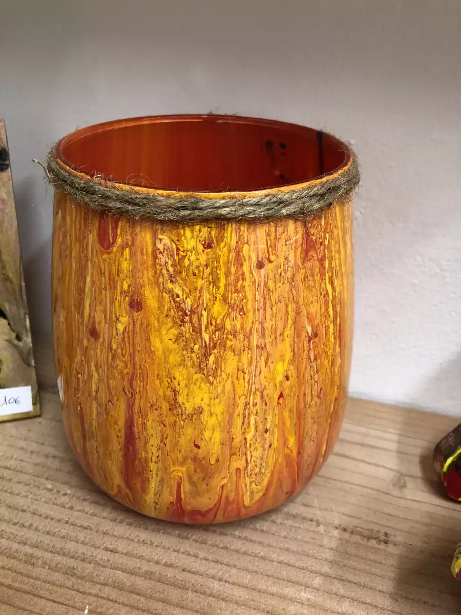 Vase artisanal marbré jaune et orange orné d'une cordelette en jute sur une étagère en bois.
