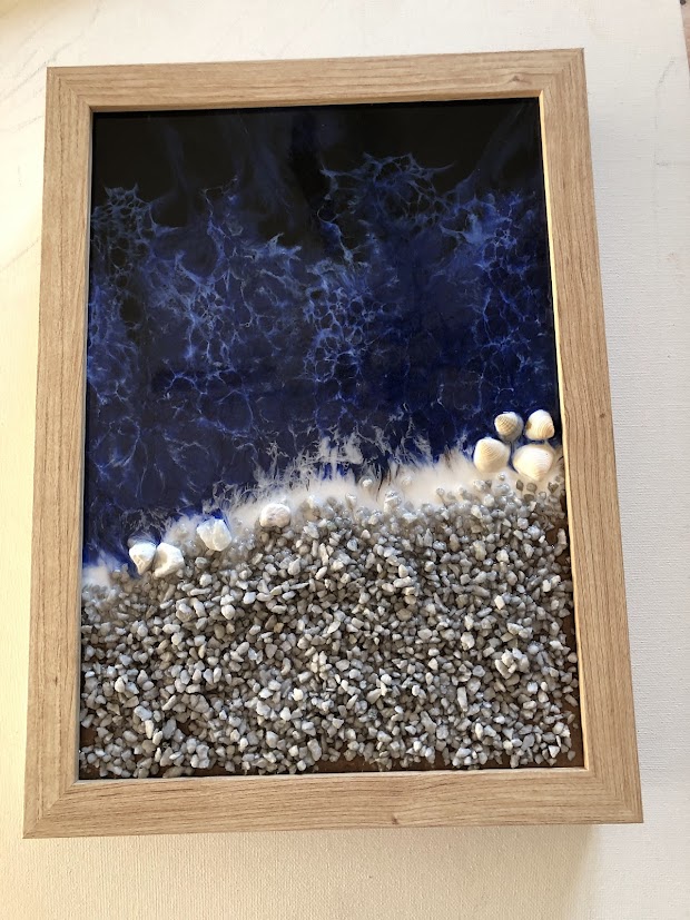 Tableau Résine Époxy Mer Bleue et Plage de Coquillages Résine époxy mer bleue avec écume blanche, coquillages et gravier gris dans un cadre en bois clair.